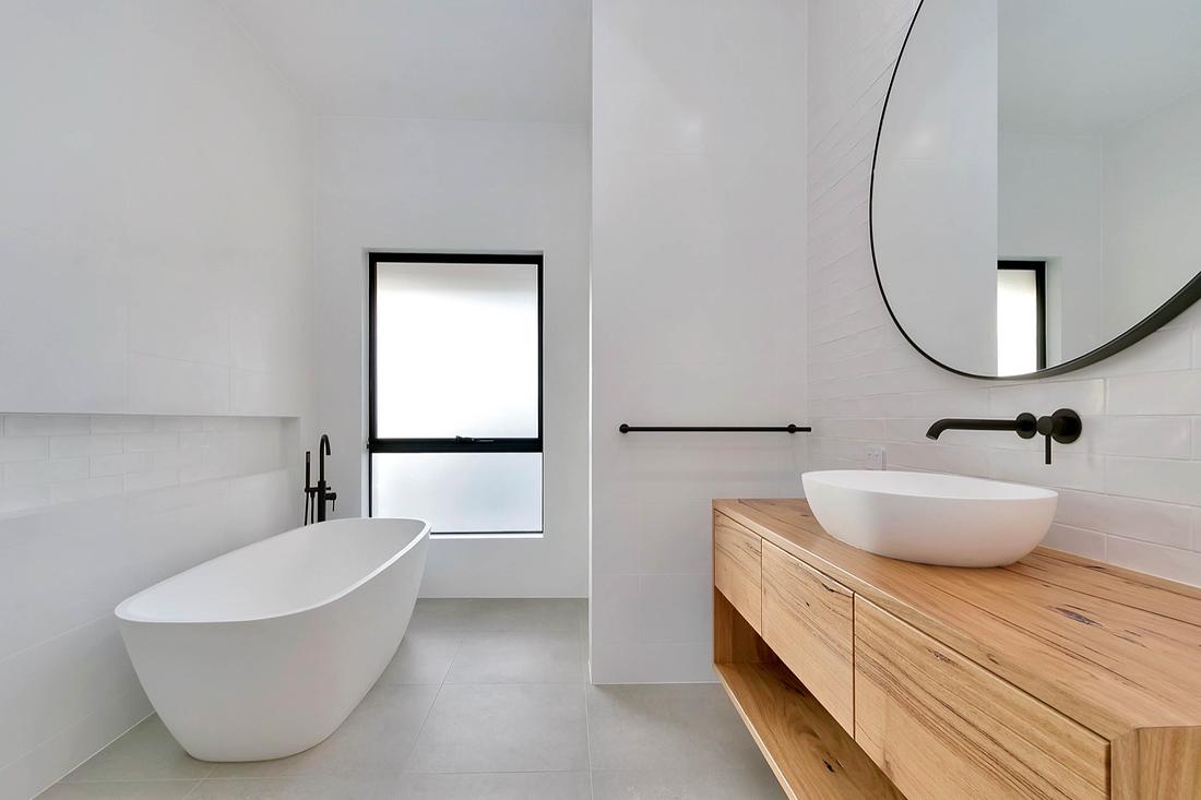 White bathroom with freestanding bath, black floor-mounted bath filler and timber vanity