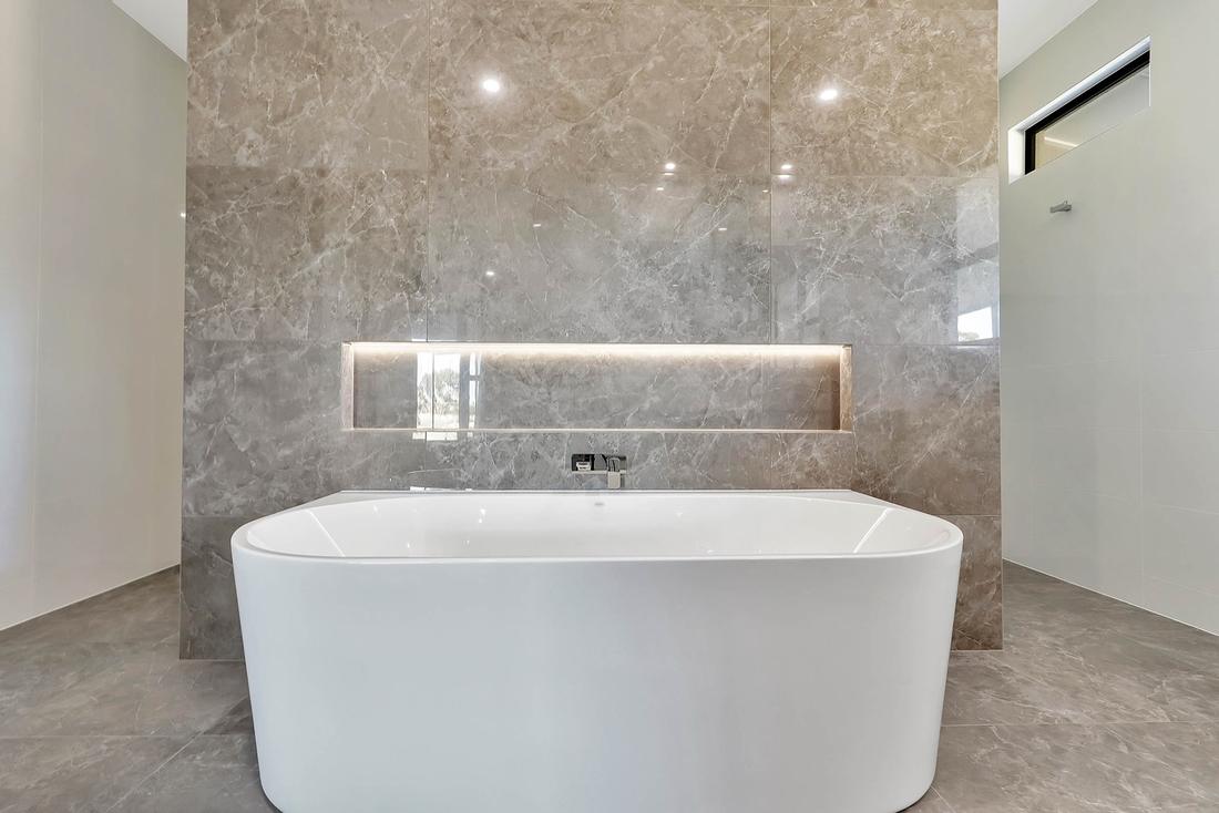 Freestanding bath against a marble-look feature wall with a lit niche