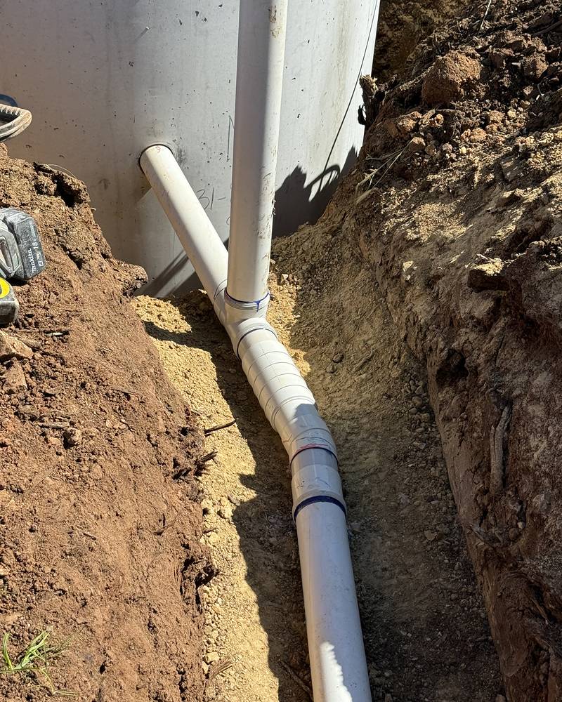 New white PVC pipework and junction running from a septic tank along a freshly dug trench