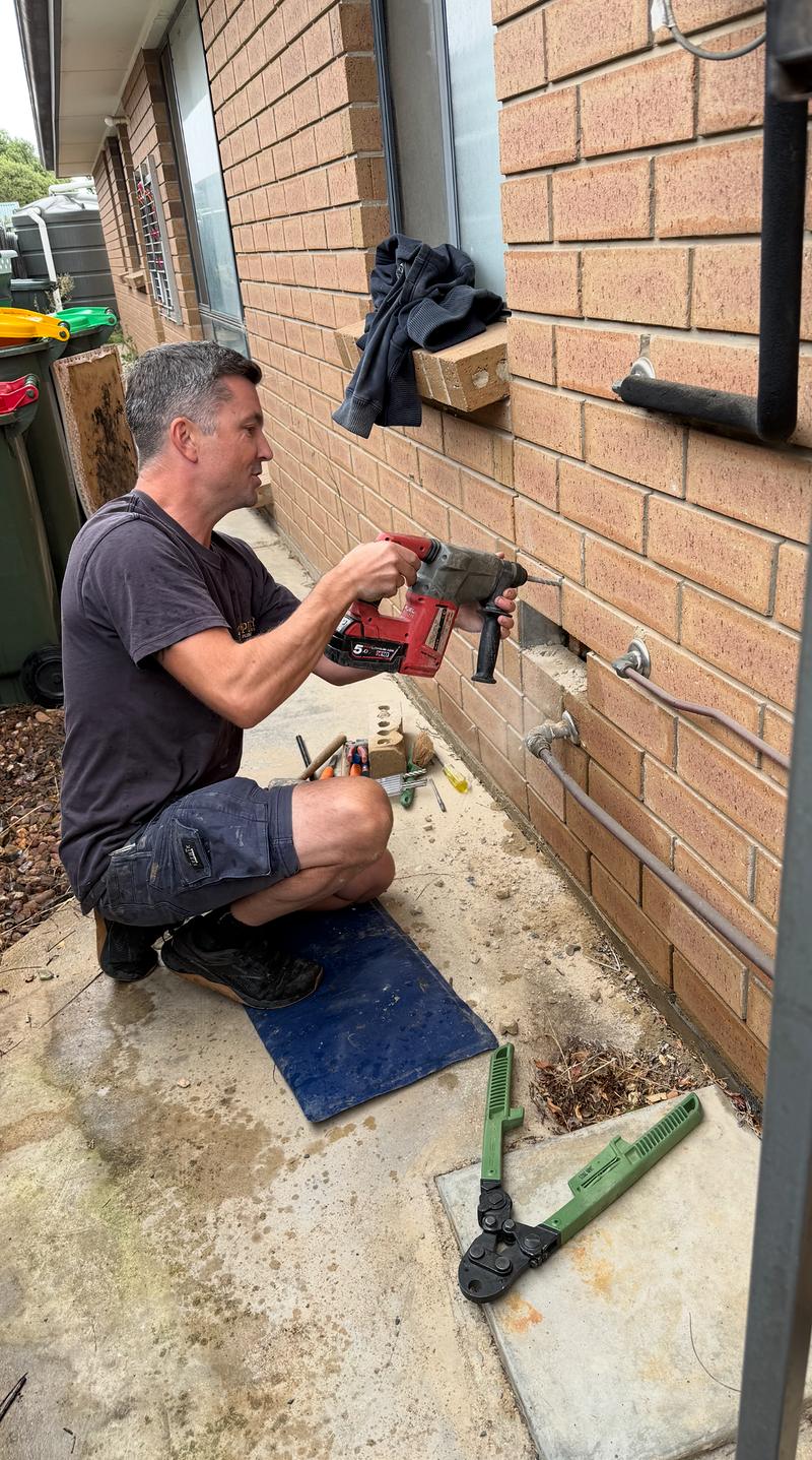 Craig drilling through a brick wall to run new pipework