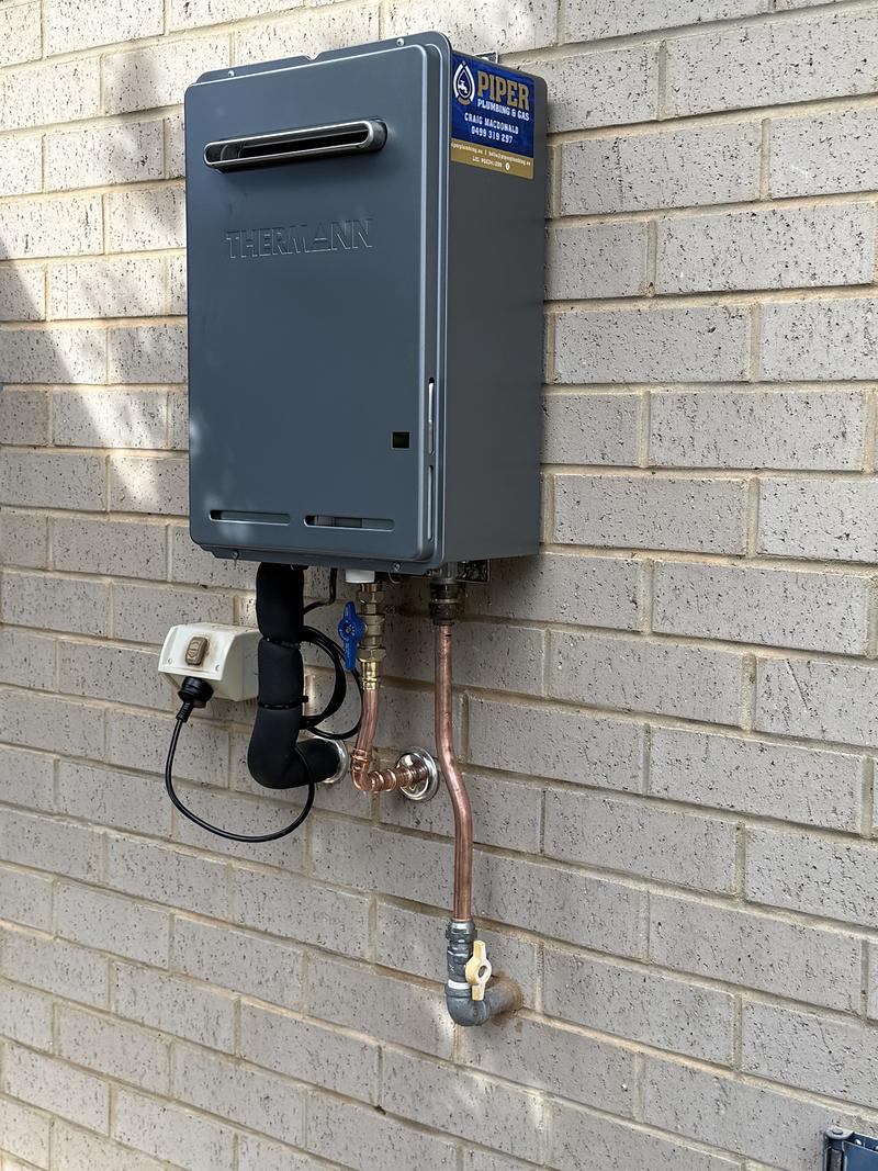 Continuous-flow gas hot water unit on a brick wall with new copper pipework