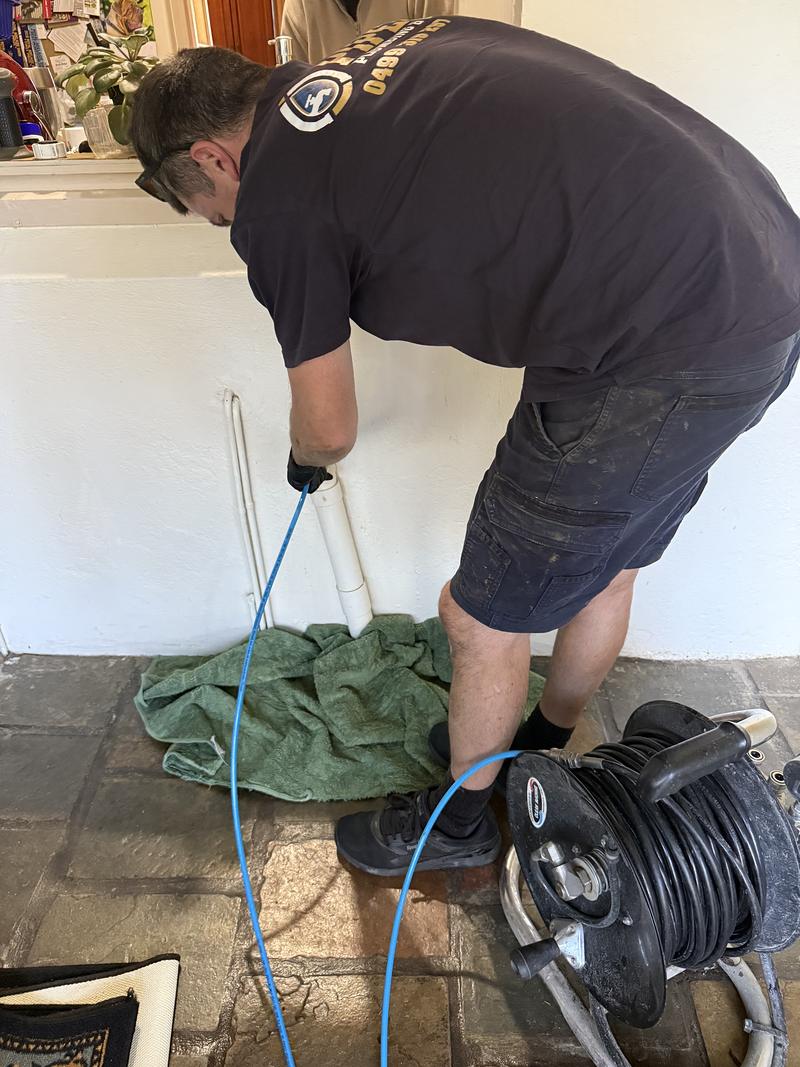 Craig clearing a blocked drain inside a house, with the drain cleaning reel beside him