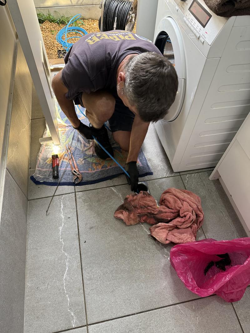 Craig clearing a laundry floor waste beside the washing machine