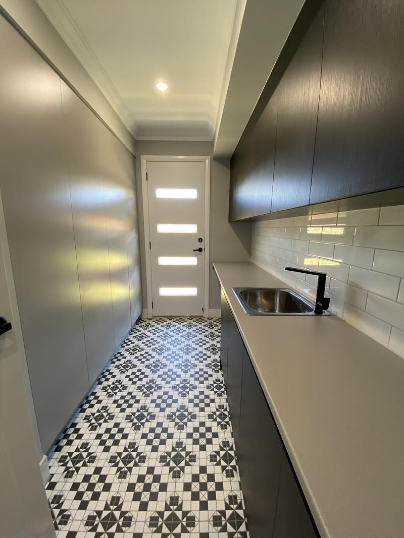 Renovated laundry with black cabinetry, patterned tile floor and black tapware
