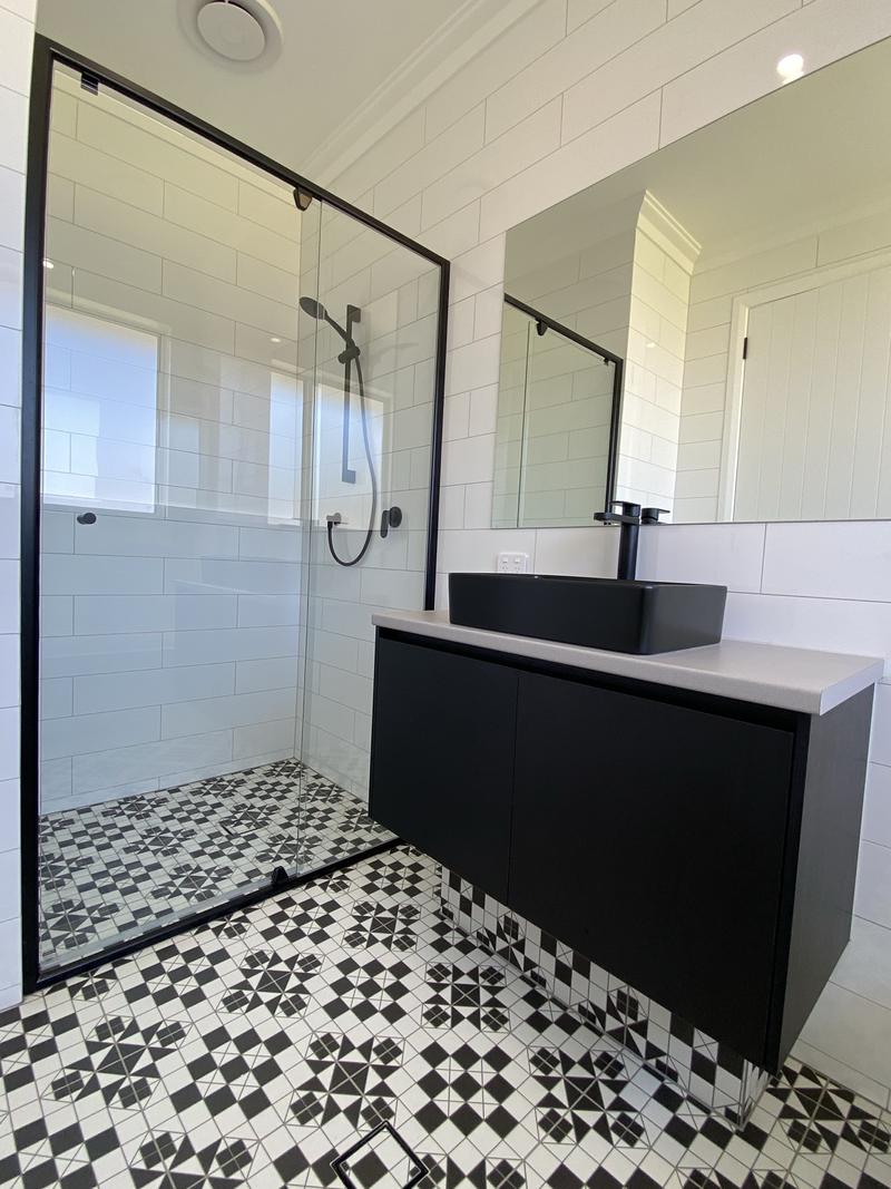 Black and white bathroom with a black-framed shower screen, black basin and patterned floor tiles