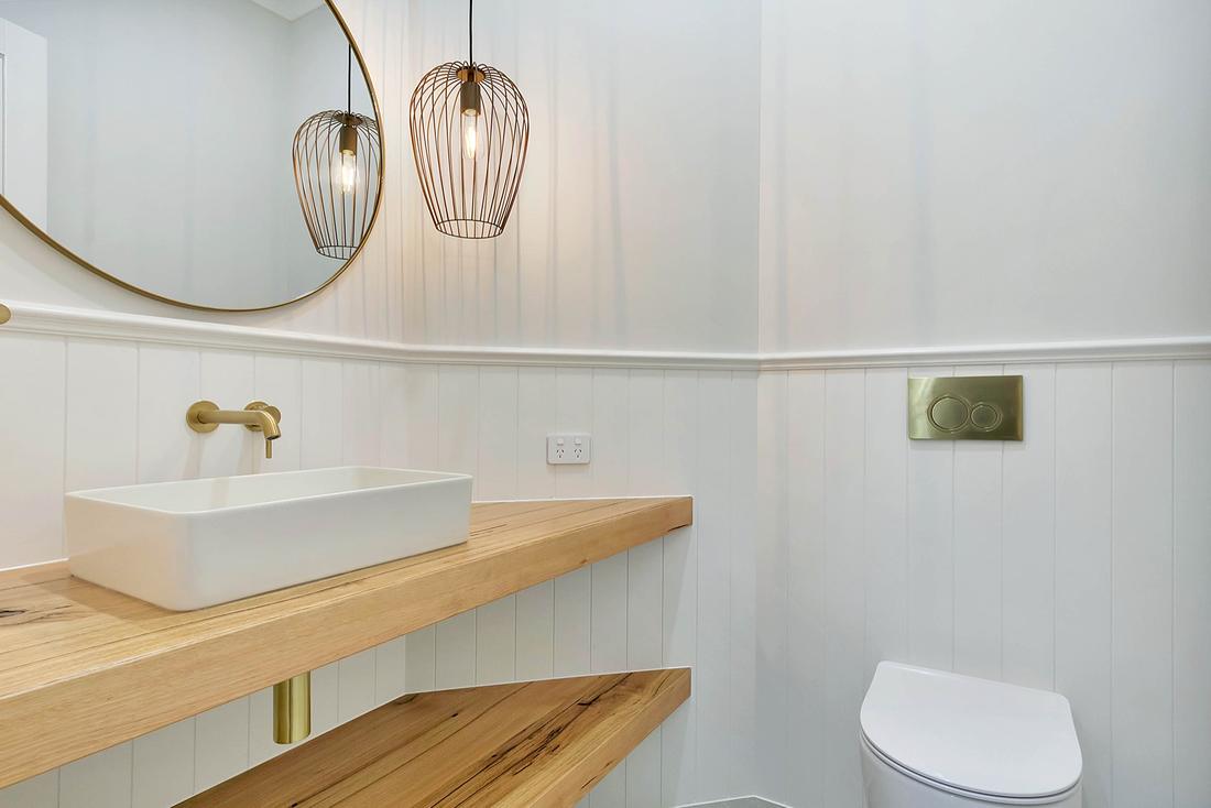 Powder room with a brass wall-mounted tap, brass flush plate and timber shelves