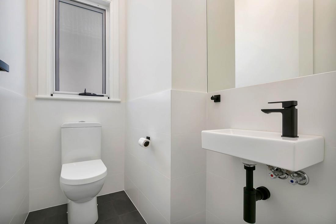 White powder room with a wall-hung basin, black bottle trap and black tapware