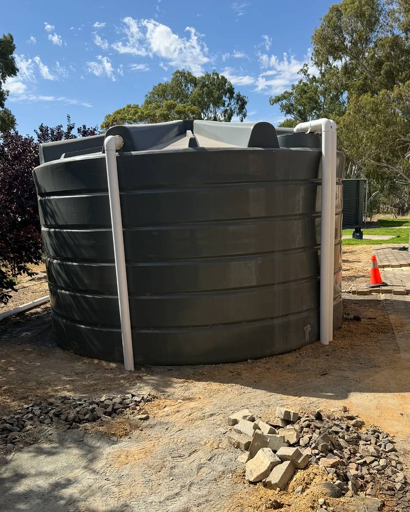 Large dark round rainwater tank with new white downpipes connected