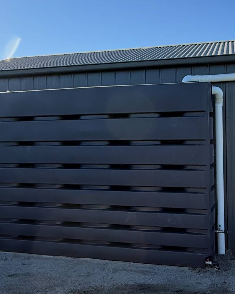 Dark slatted screen in front of a rainwater tank beside a shed