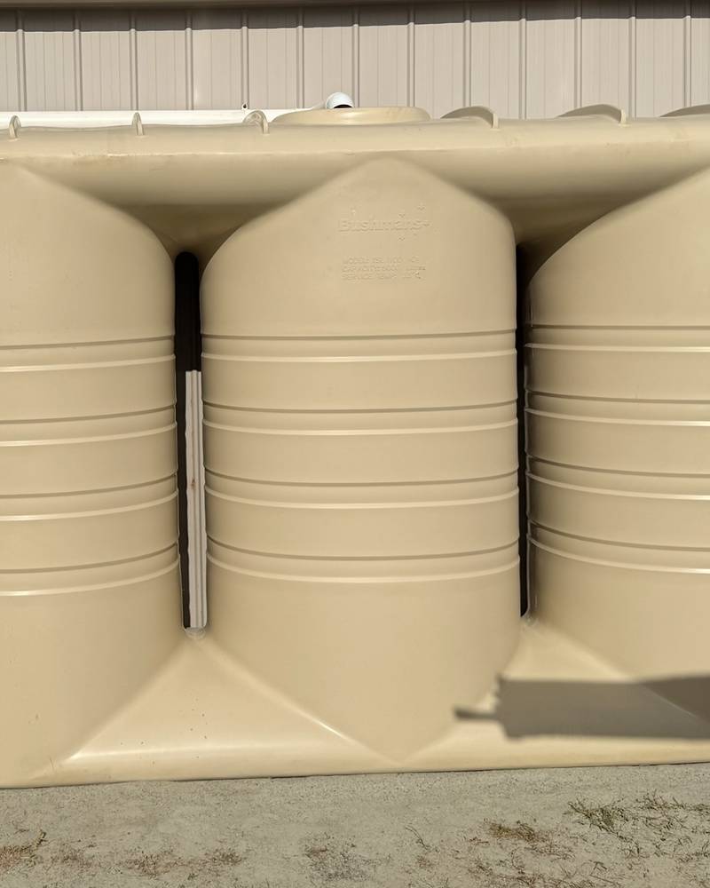 Three linked beige slimline rainwater tanks against a shed wall