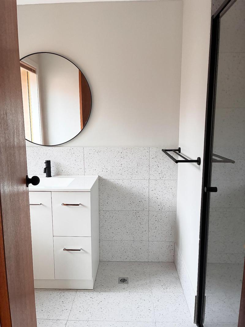 Bathroom with a round mirror, white vanity and black towel rail