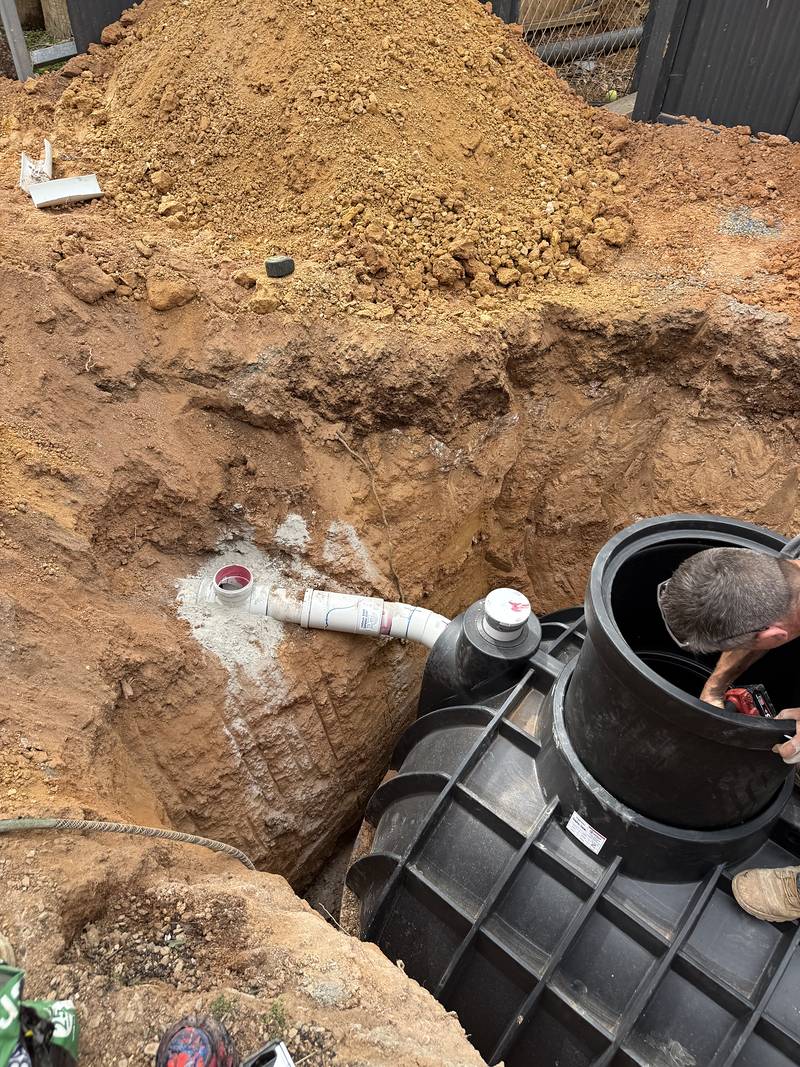 New black septic tank sitting in a freshly dug hole with a PVC pipe connected