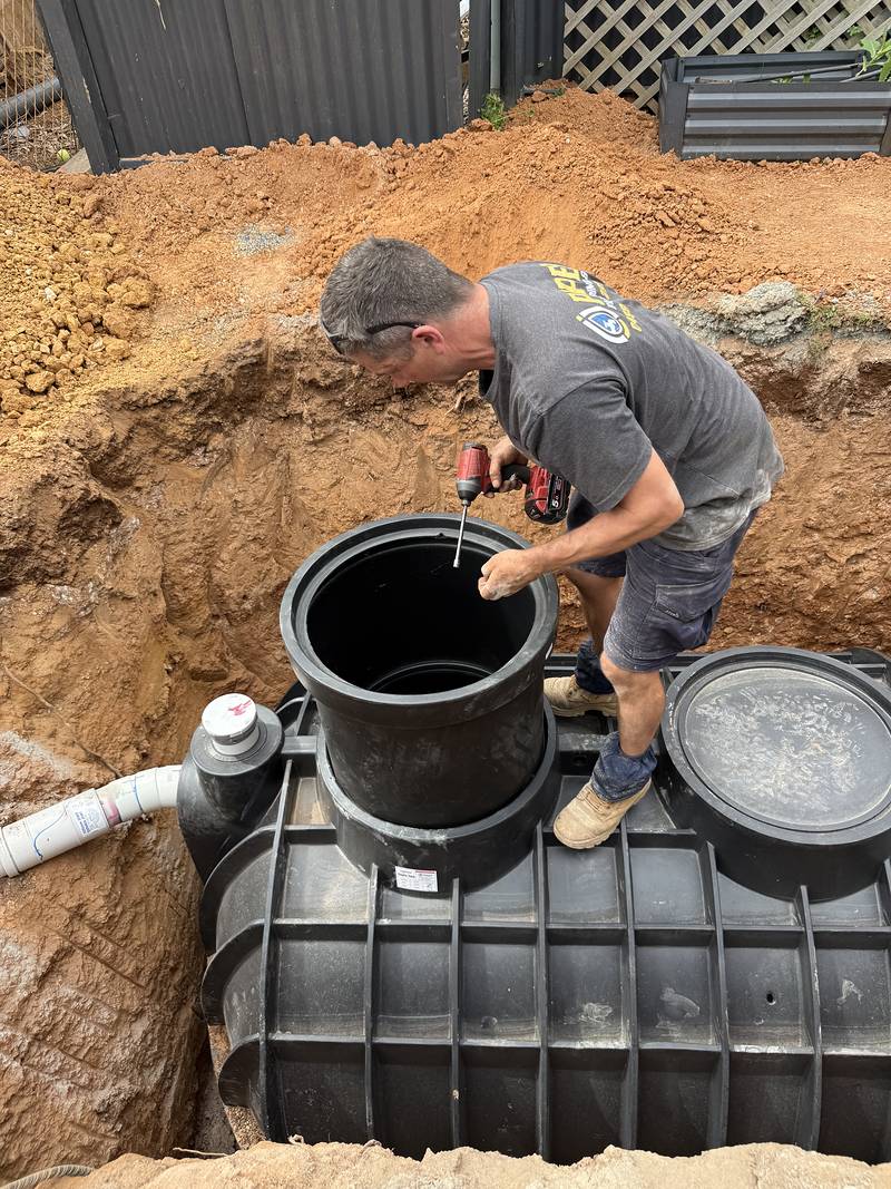 Craig standing on the septic tank with a drill, fitting a riser to the tank opening
