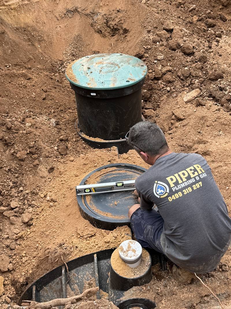 Craig checking a septic tank lid with a spirit level, a green-lidded riser behind him