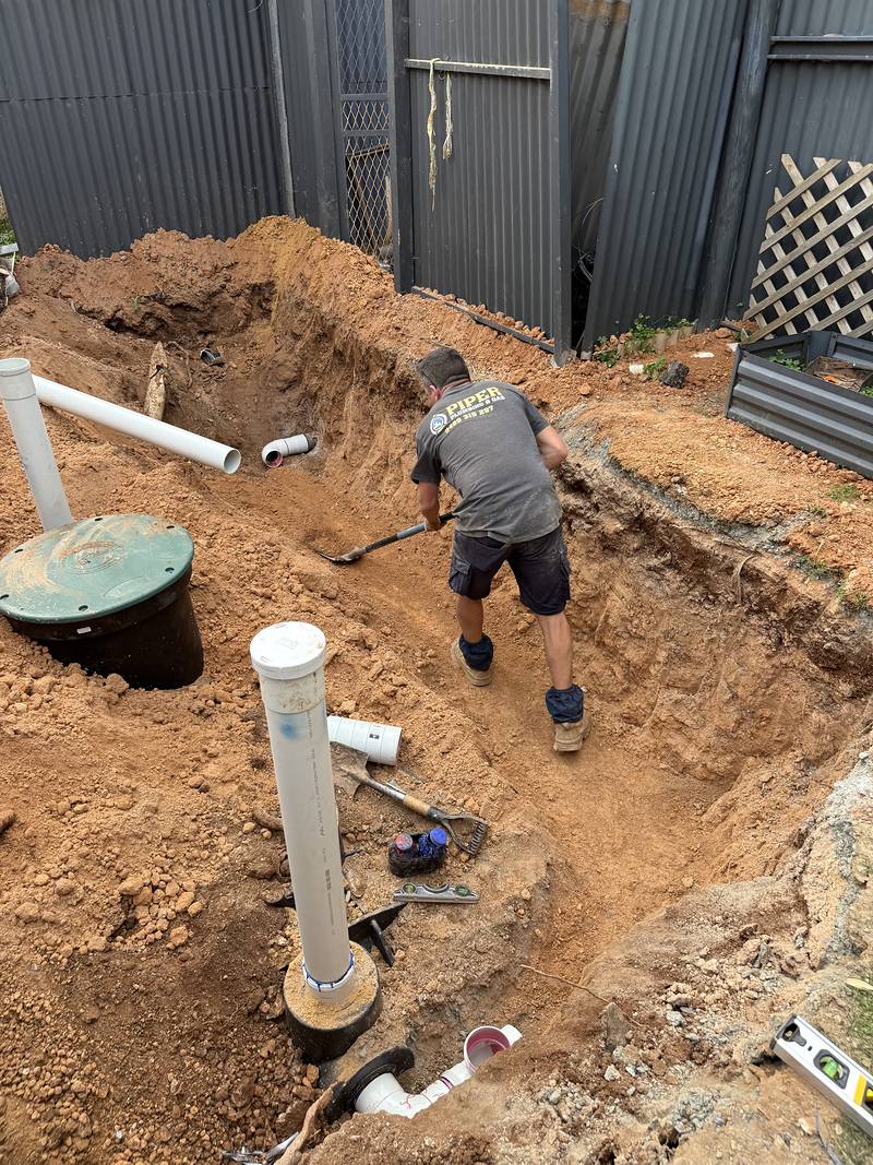 Craig digging out a wide trench in a backyard beside the tank risers