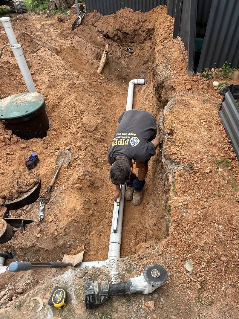 Craig in the trench laying a run of white PVC pipe