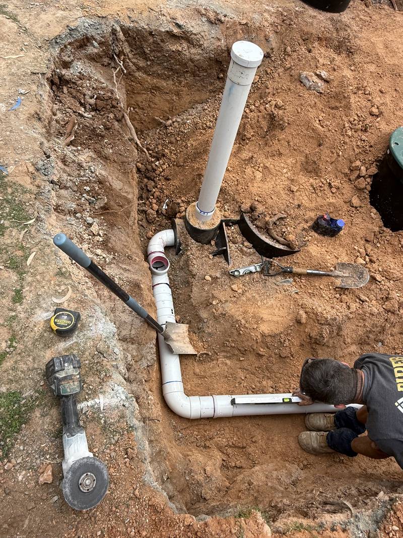 Craig lying beside the trench checking the new PVC pipe with a spirit level