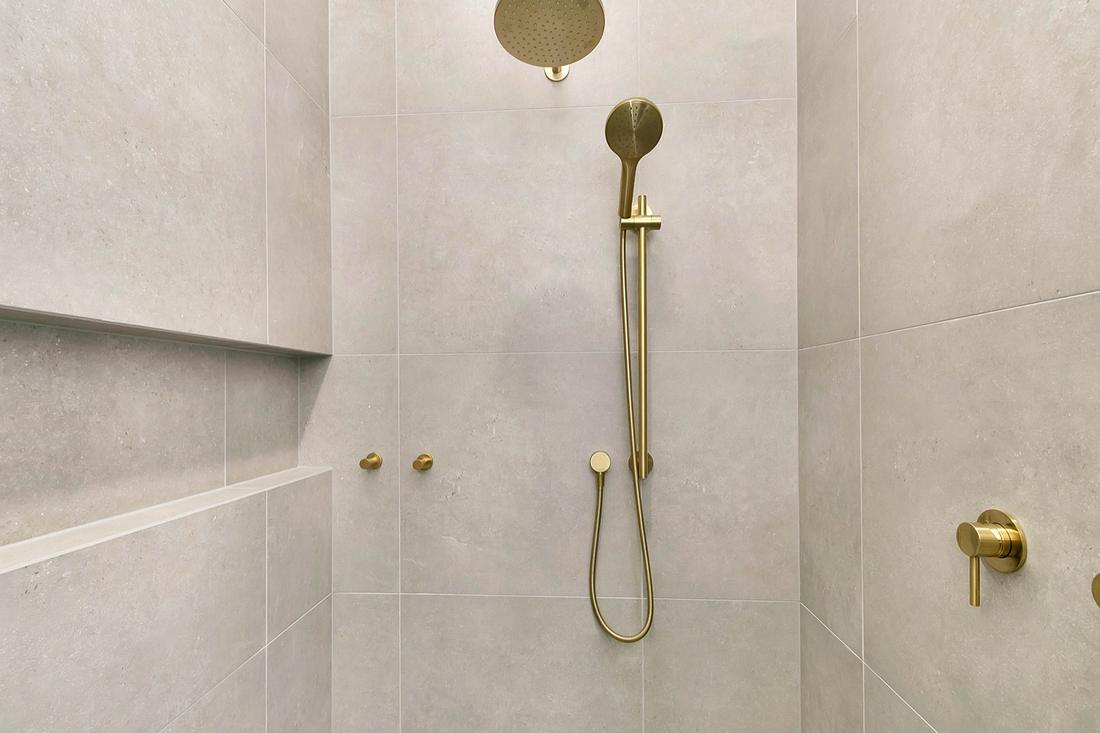 Stone-look tiled shower with brushed brass rain head, hand shower and niche