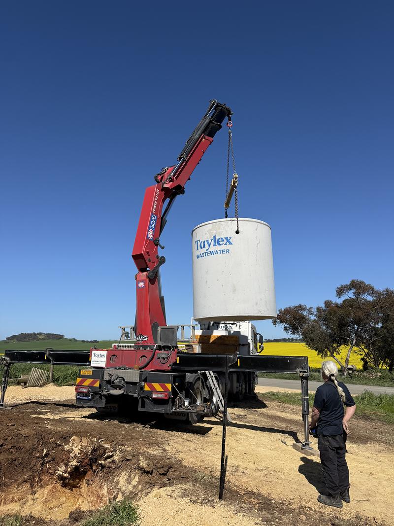 Crane truck lowering a wastewater tank into place on a rural block