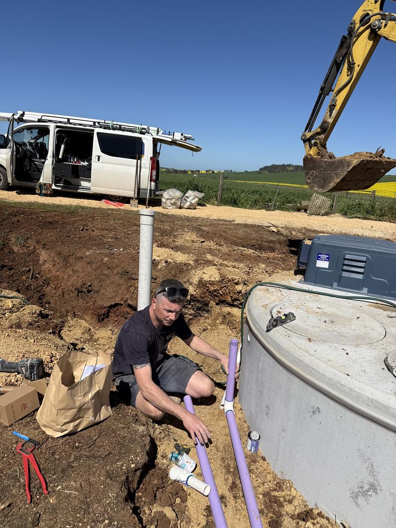 Craig plumbing in an aerobic wastewater tank, with the van and an excavator behind