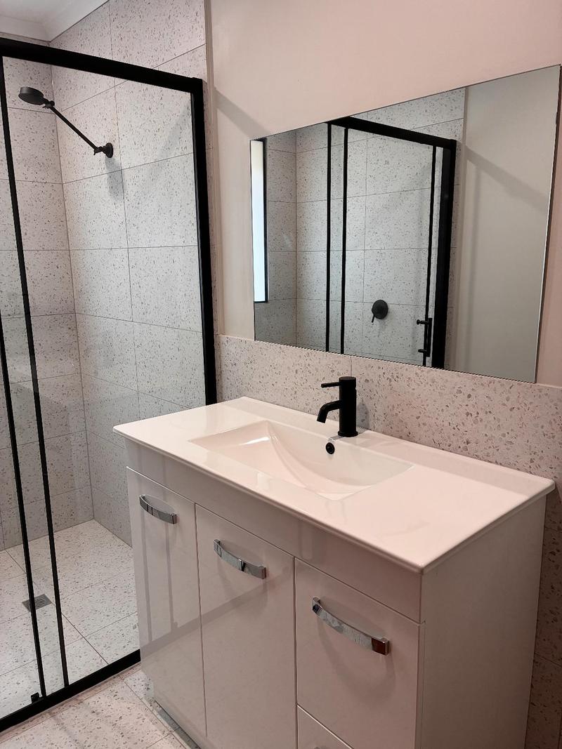 Finished vanity with basin mixer and mirror beside a black-framed shower