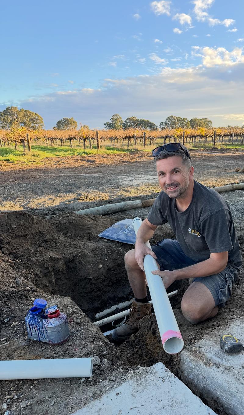 Craig in a trench beside a vineyard with a length of new PVC pipe
