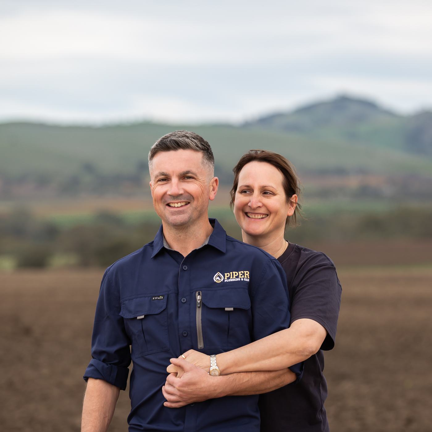 Craig and Hayley of Piper Plumbing & Gas in a Barossa paddock, hills behind
