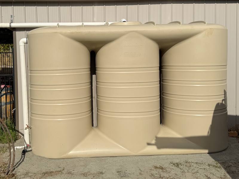 Three linked slimline rainwater tanks installed against a shed wall