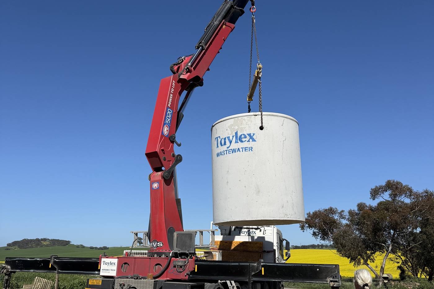 Crane truck lowering a new wastewater tank into place on a rural block