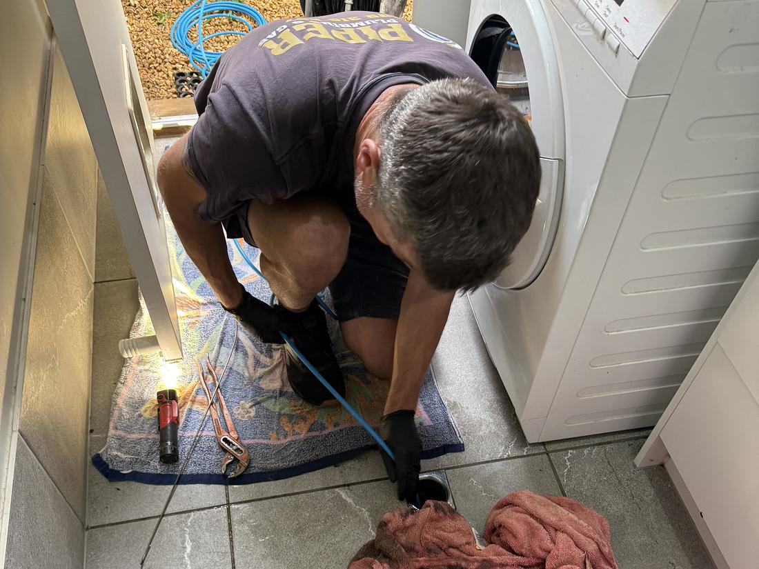 Craig clearing a laundry floor waste beside the washing machine