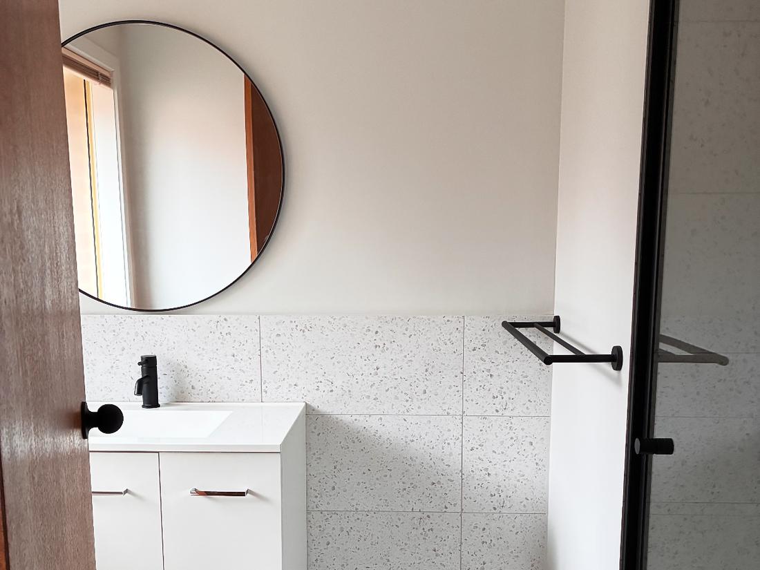 Finished bathroom with a white vanity, round mirror and black tapware