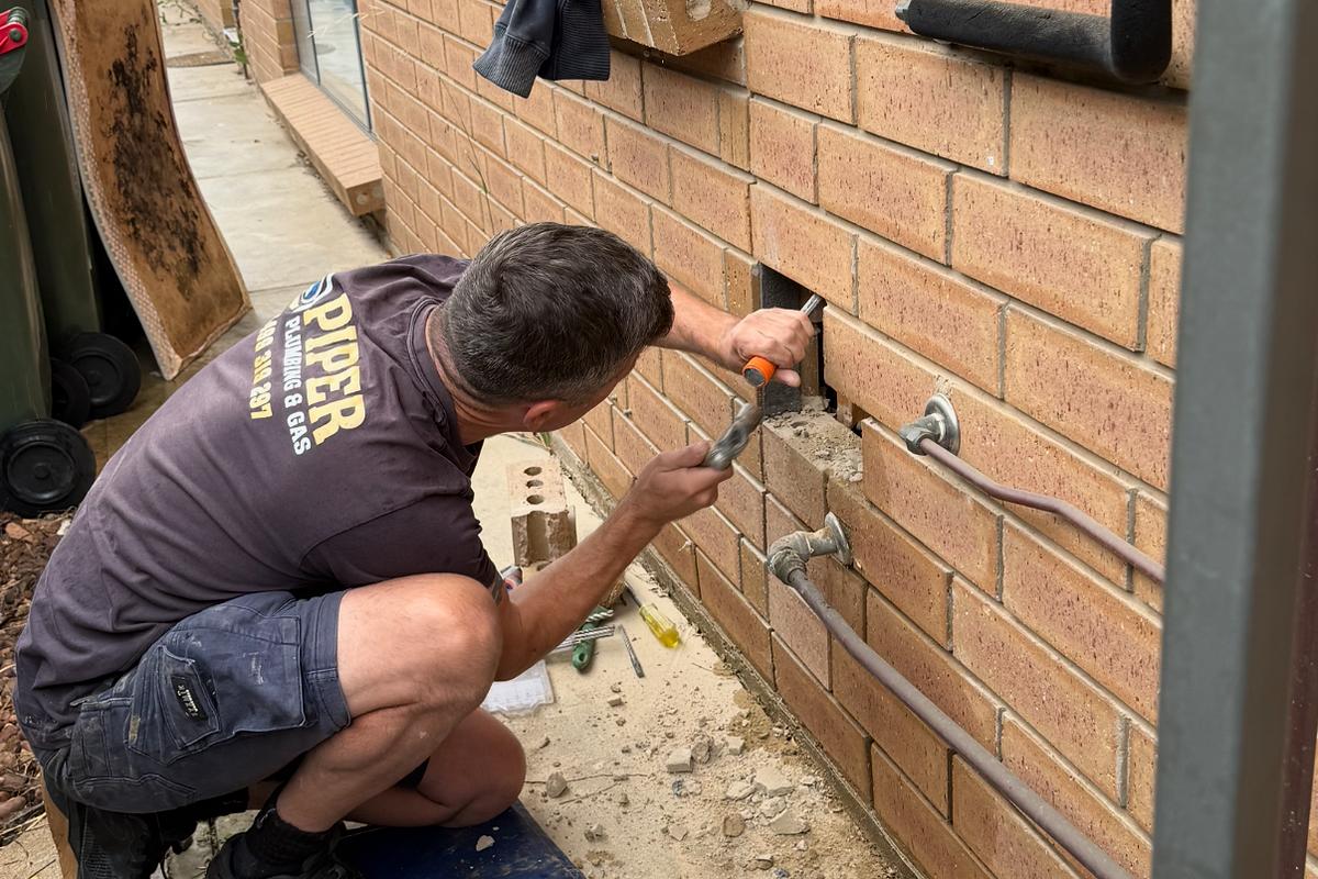 Craig drilling through a brick wall to run new pipework
