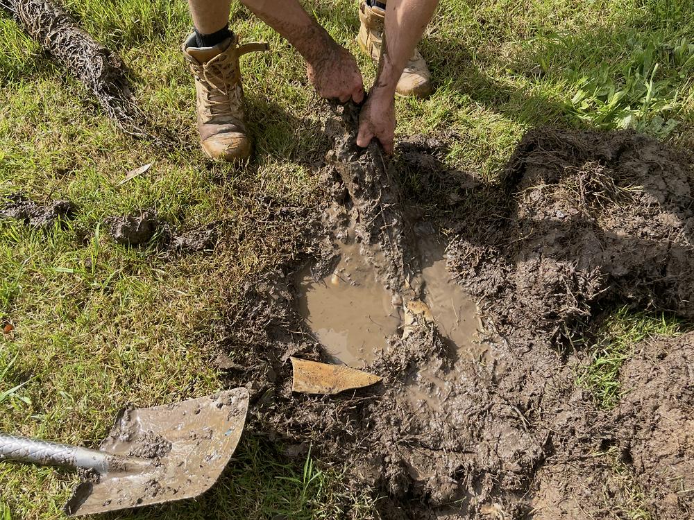 A drain dug up in a lawn with a shovel beside the hole