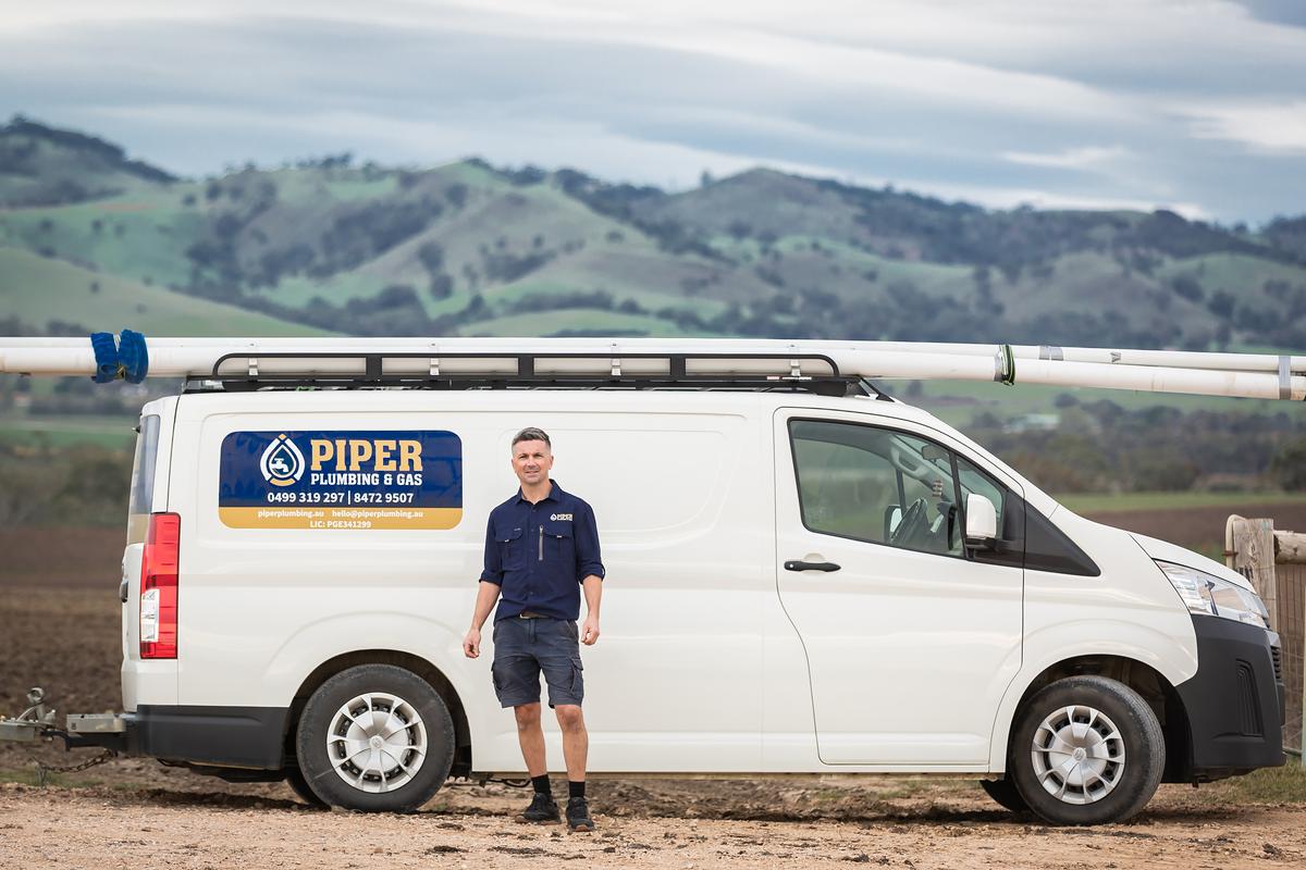 Craig beside the signwritten Piper Plumbing & Gas van with the Barossa hills behind