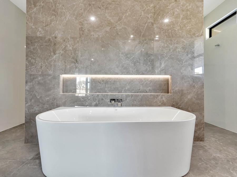 Freestanding bath in front of a stone-look feature wall with a lit niche and a wall-mounted bath tap