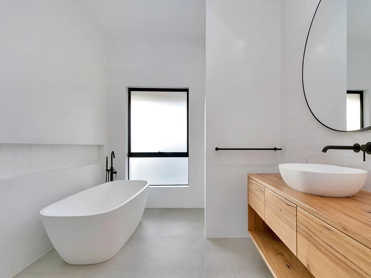 Freestanding bath with a black floor-mounted tap beside a timber vanity