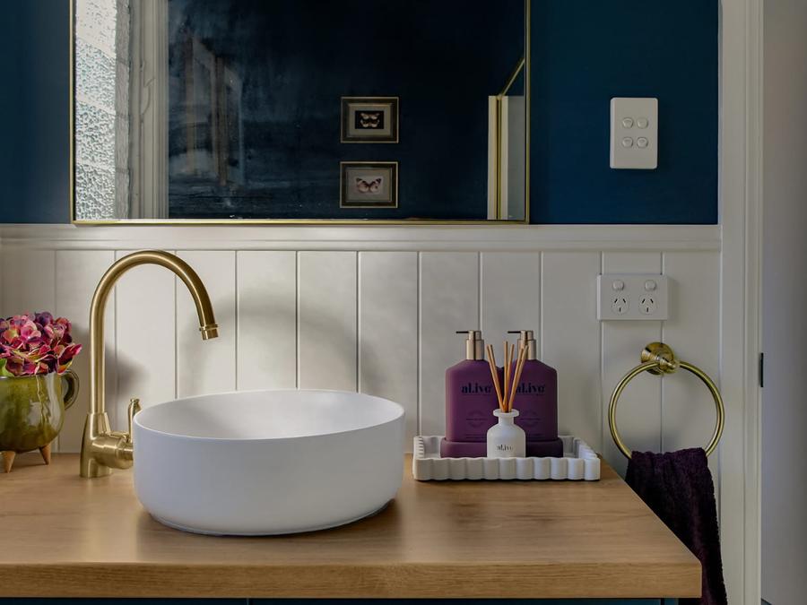 Round basin on a timber top with a brass gooseneck tap and navy walls