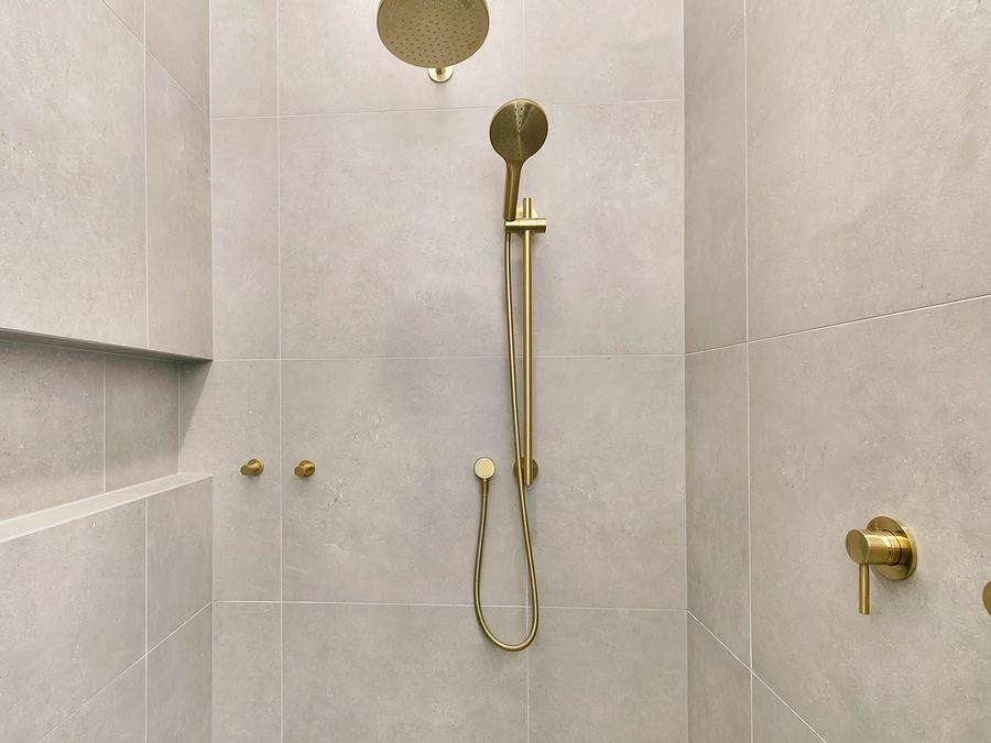 Tiled shower with a brushed brass rail shower, wall mixer and niche