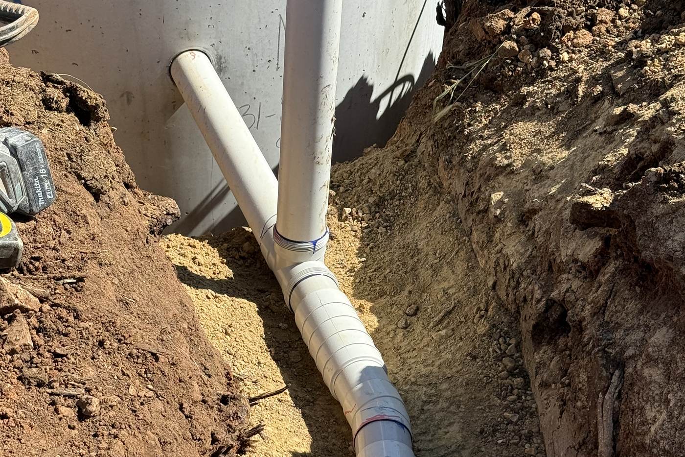 New white PVC pipework and junction running from the septic tank along a freshly dug trench