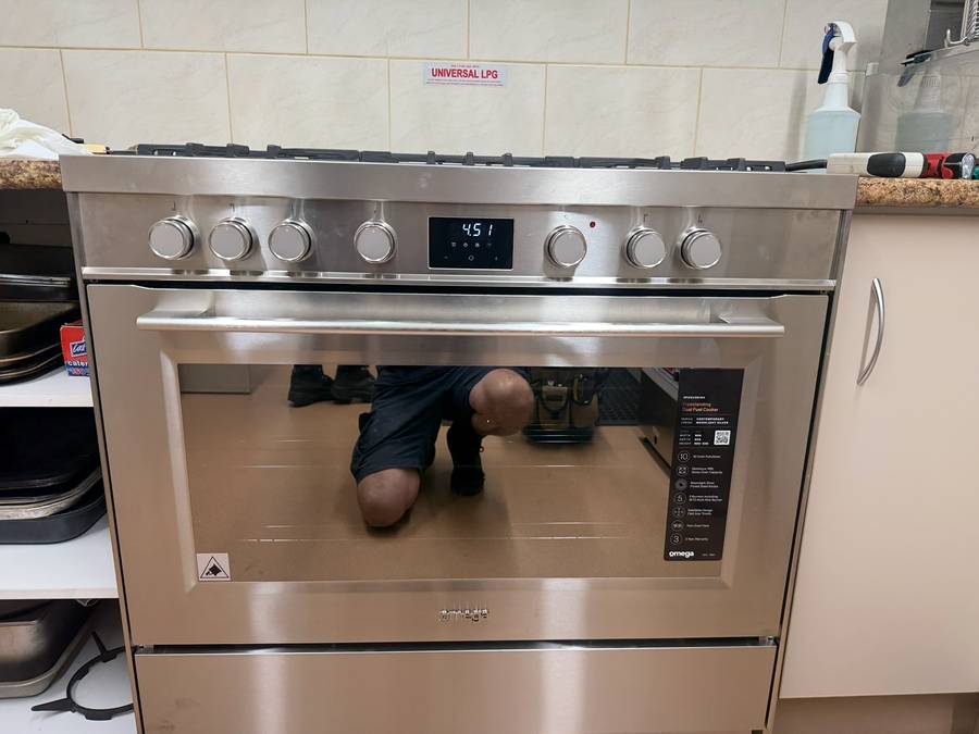 Stainless steel freestanding gas oven and cooktop installed between kitchen cupboards, LPG sticker on the wall above