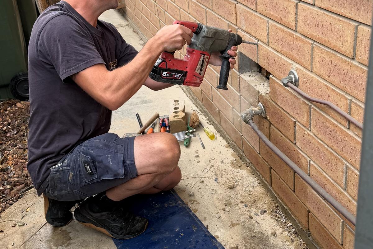Craig drilling through a brick wall to run new pipework