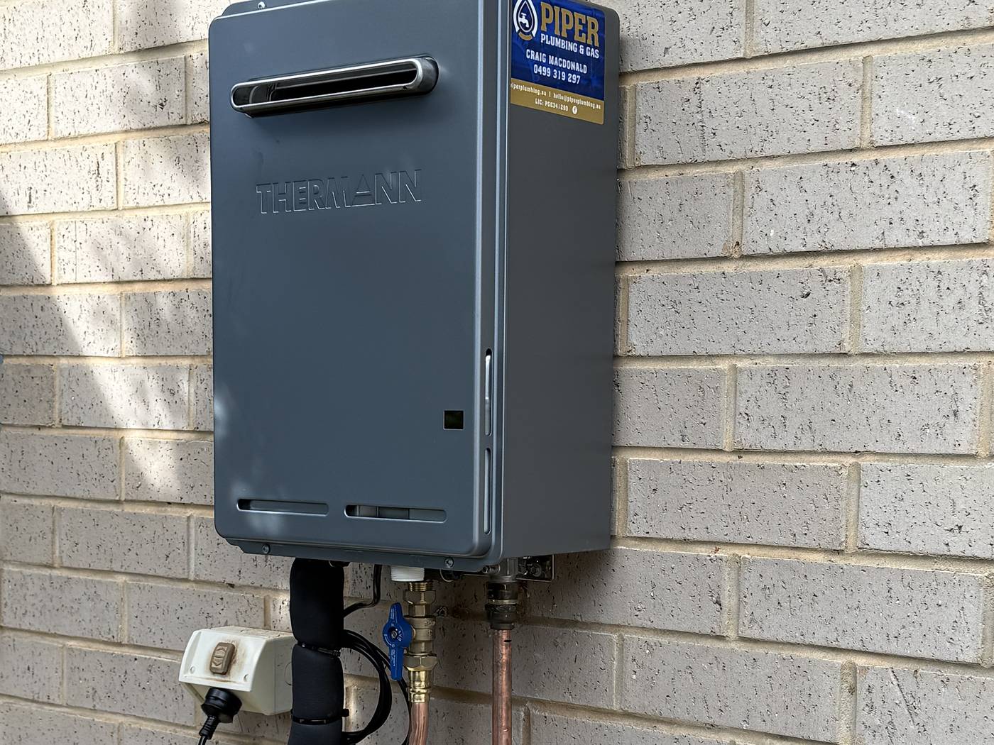 Continuous-flow gas hot water unit installed on a brick wall with new copper pipework below it