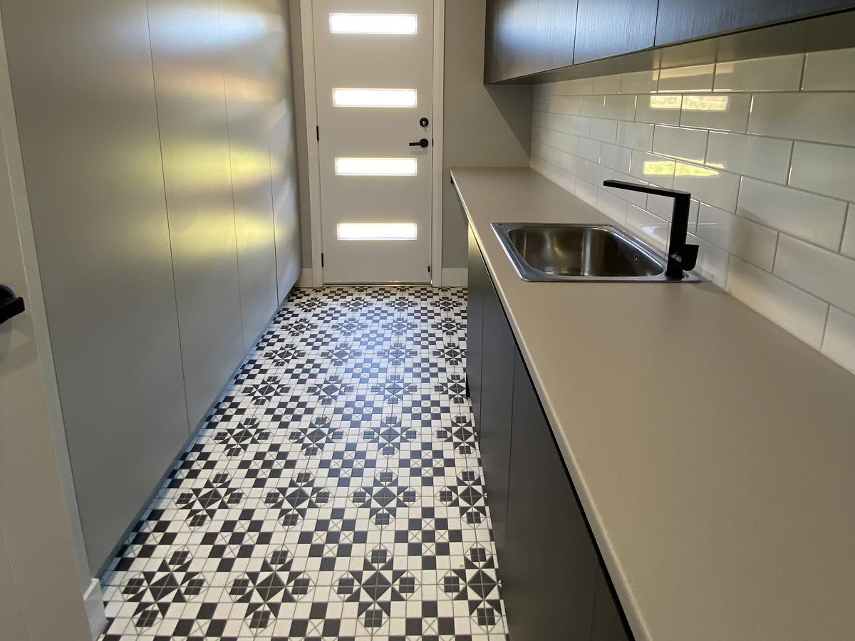 Renovated laundry with black cabinets, a stone bench and patterned floor tiles