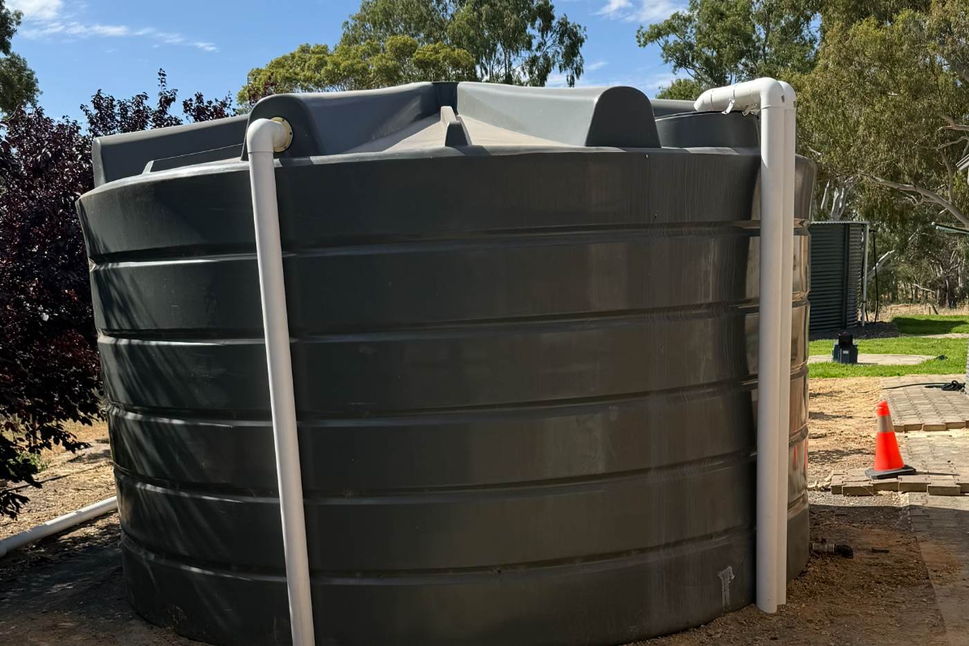 Large dark round rainwater tank installed on a cleared site, with new white downpipes connected