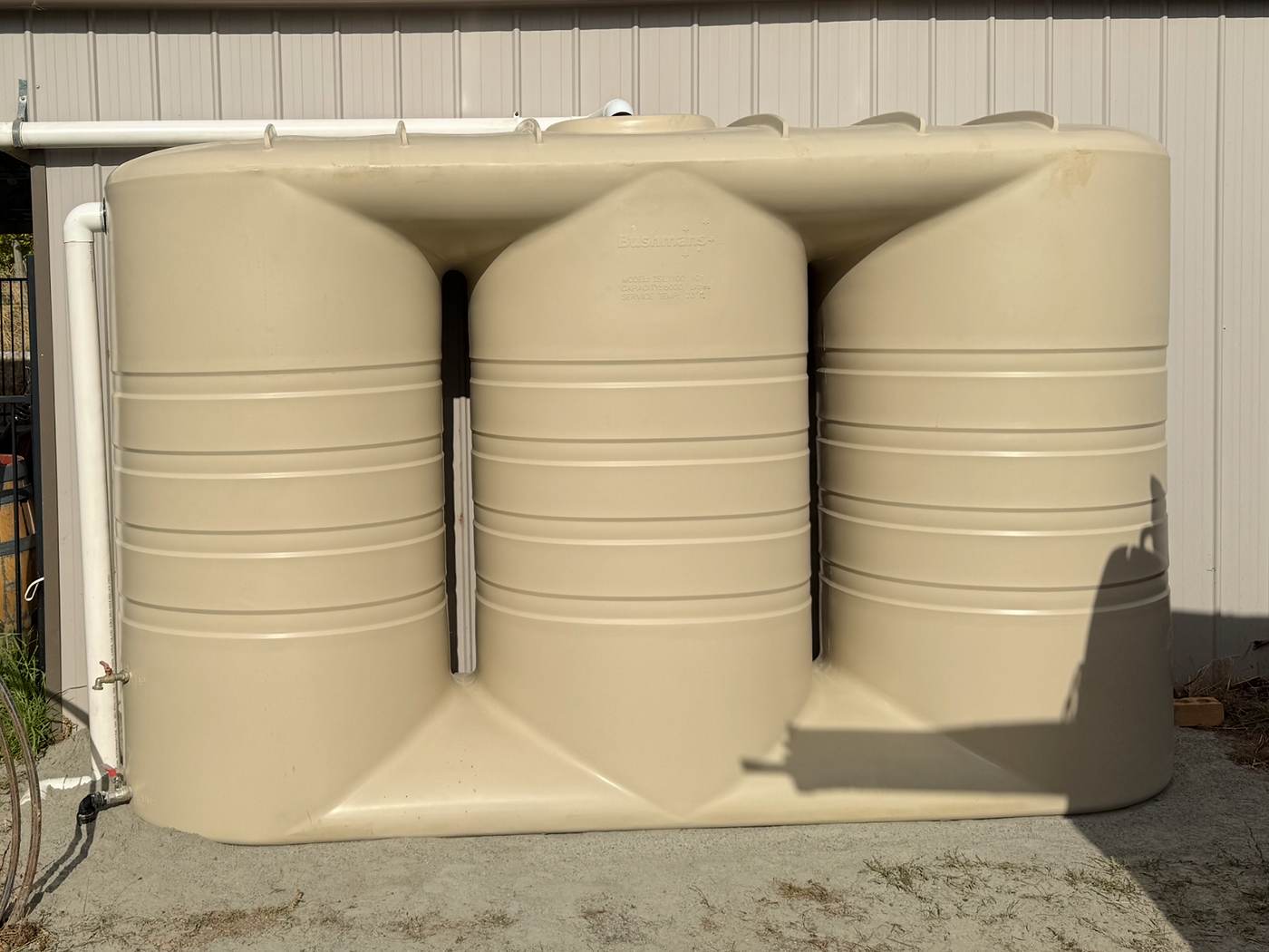 Three linked beige slimline rainwater tanks installed against a shed wall, with new pipework along the top