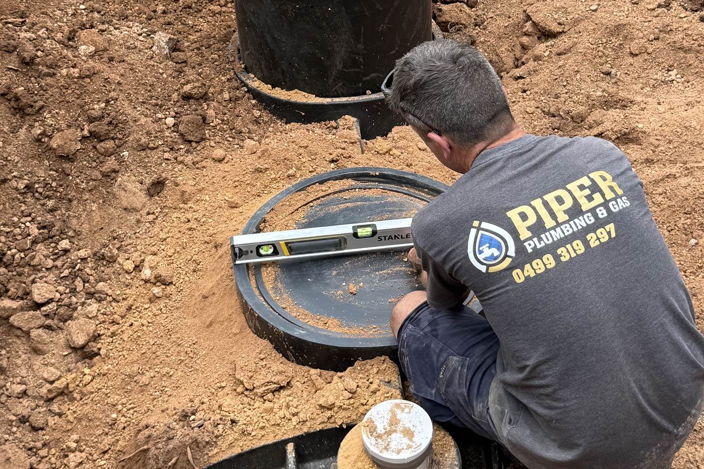 Craig in a Piper Plumbing shirt checking a septic tank lid with a spirit level