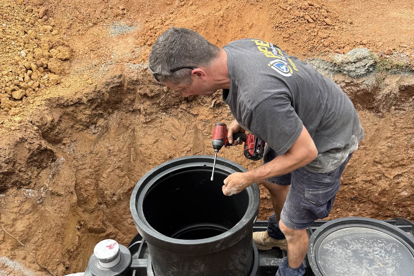 Craig from Piper Plumbing & Gas fitting a riser to a new septic tank in a red-soil hole