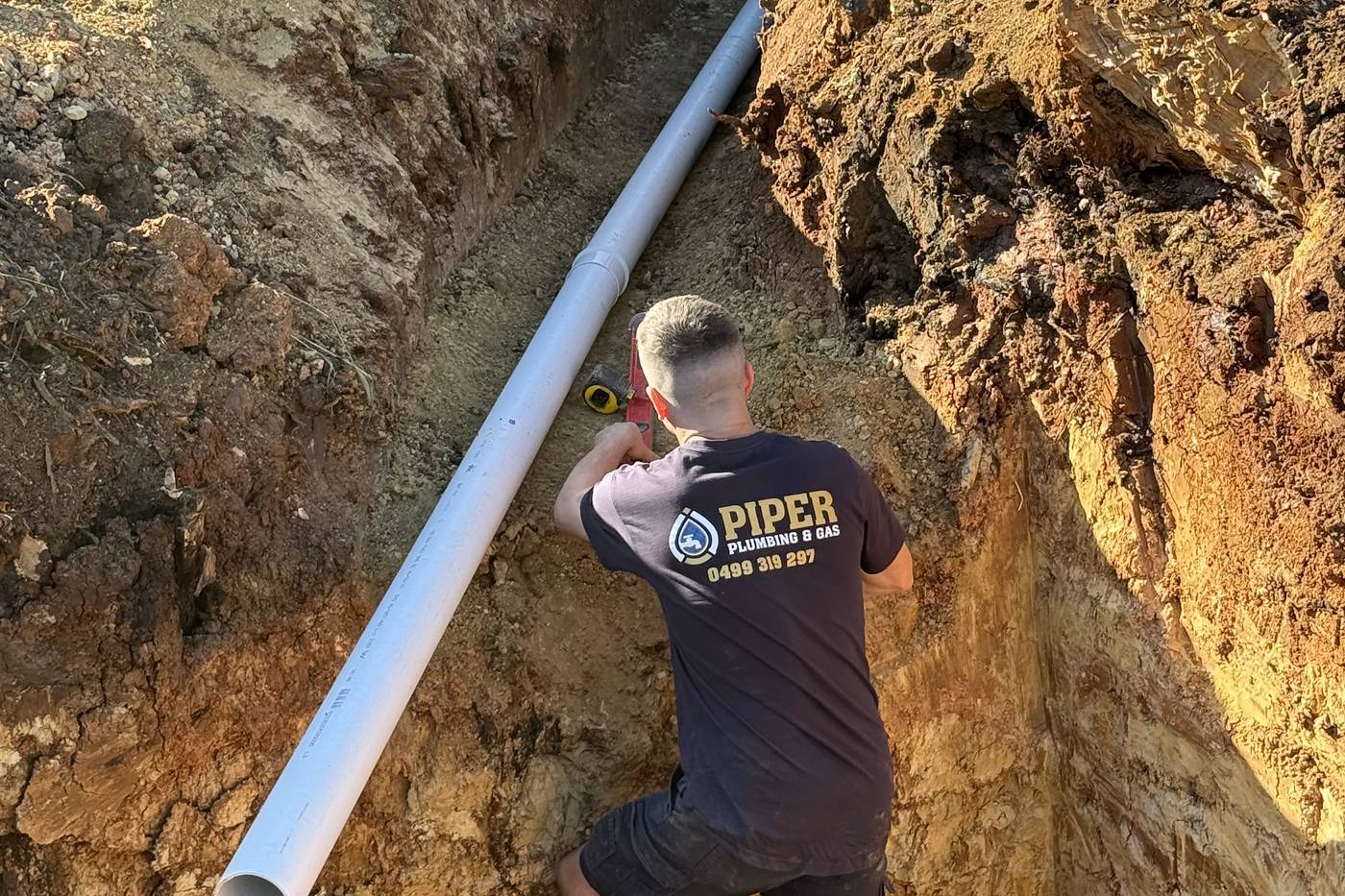 Craig laying new PVC sewer pipe at the bottom of a deep trench