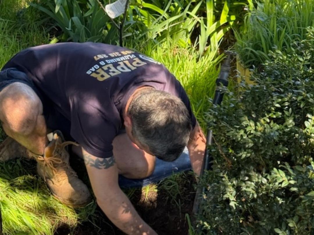 Craig digging down to a blocked drain in an overgrown garden bed