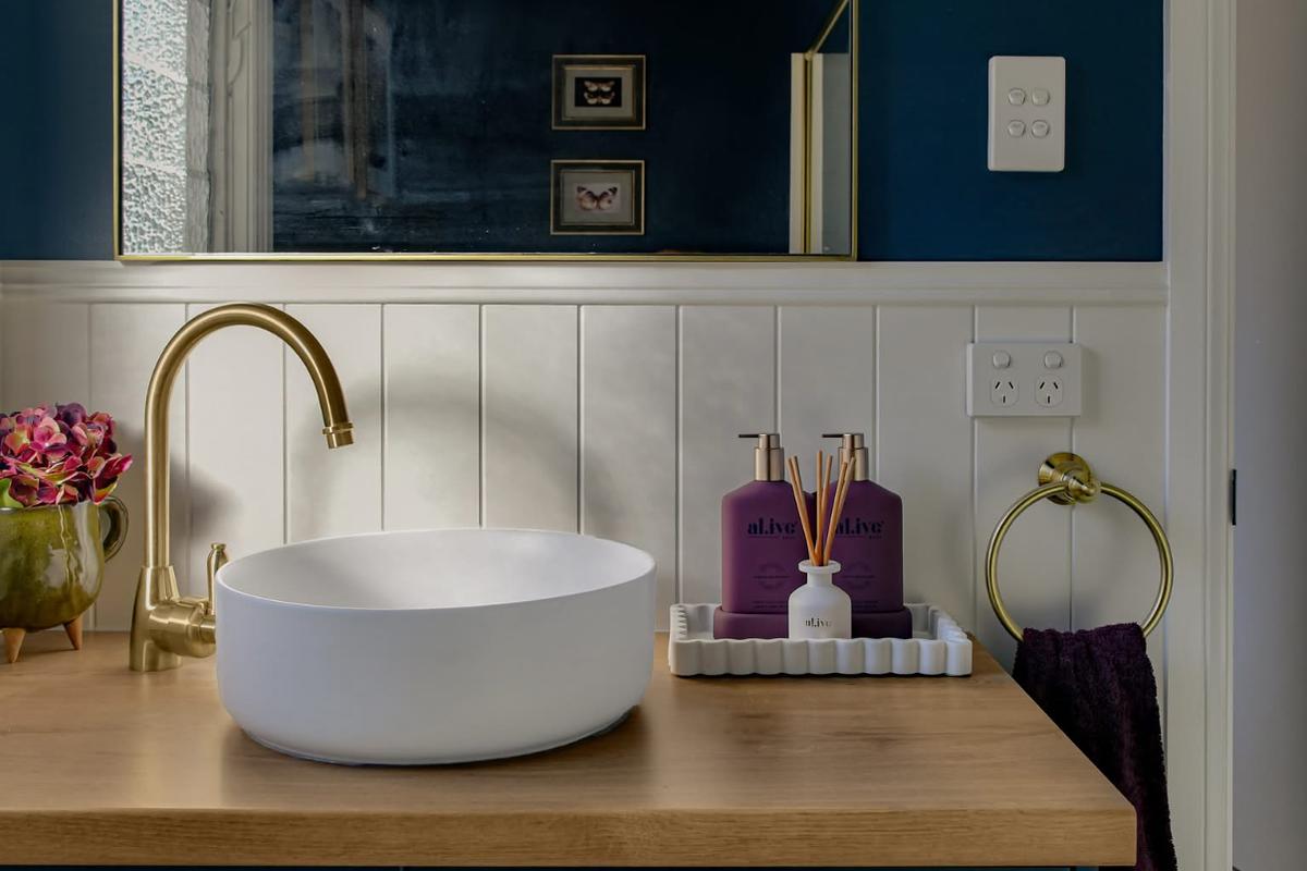 Round basin on a timber top with a brass gooseneck tap and navy walls
